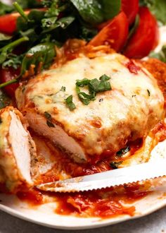 a white plate topped with meat covered in sauce next to greens and tomato wedges