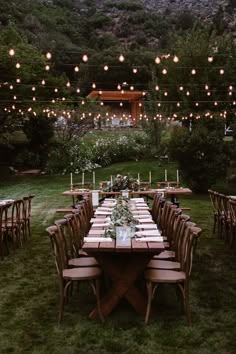 an outdoor dinner table set up with candles and greenery on the lawn, surrounded by string lights