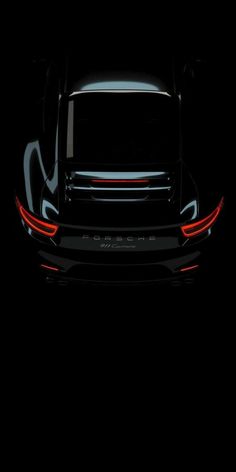 the rear end of a black sports car with its lights turned on in the dark