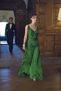 a woman in a green dress is standing on the floor with her hands behind her back