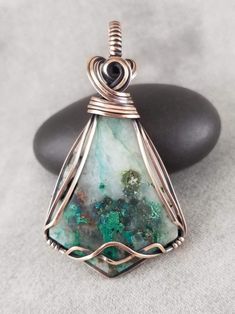 a wire wrapped pendant sitting on top of a rock next to a black stone with green and white designs