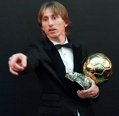 a man in a tuxedo holding a soccer ball and pointing at the camera