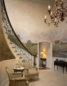 two chairs and a table in front of a staircase with paintings on the wall behind them