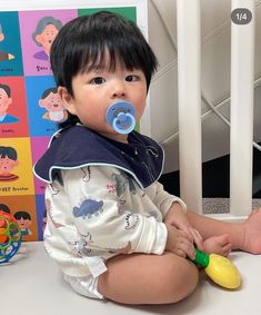 a baby sitting on the floor with a pacifier in his mouth and wearing a bib