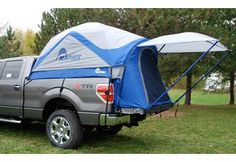 a truck with a tent attached to it's bed parked in the grass near some trees