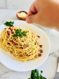 a plate of spaghetti with bacon and parsley garnish on it, being held by a person