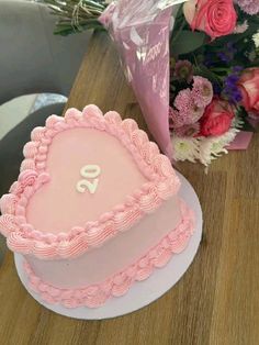 a pink heart shaped cake sitting on top of a wooden table next to a bouquet of flowers