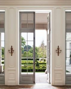 an open door leading to a garden with hedges in the back ground and large windows on either side