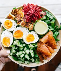 a person holding a bowl filled with salad and hard boiled eggs on top of cucumbers