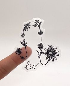 a hand holding up a sticker with the word leo written on it and flowers