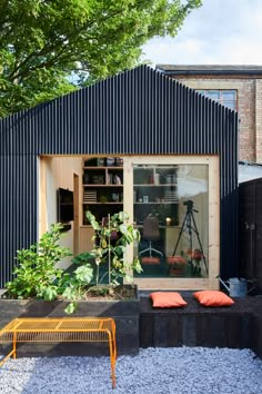 an outdoor space with plants and benches in the foreground, next to a black building