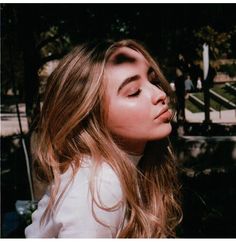 a woman with long hair and eyes closed standing in front of some stairs, looking up at the sky