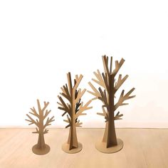 three wooden trees are standing in the middle of a room with white walls and wood flooring