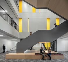 two people sitting on benches in an open space with stairs and yellow lights above them