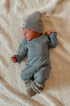 a baby laying on top of a bed wearing a gray knitted outfit and hat