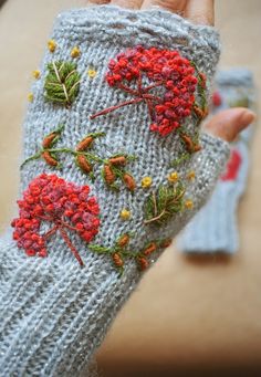 a hand holding a knitted mitt with red flowers on it and green leaves