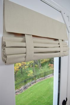 a close up of a window with a curtain on it's side and grass in the background