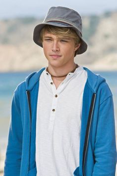 a young man wearing a hat standing next to the ocean