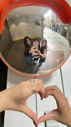 two women making a heart shape with their hands in front of a mirror that is shaped like a heart