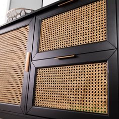 a black cabinet with gold handles and wicker design on the front, along with a mirror above it