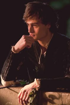 a young man sitting at a table with his hand on his chin and looking off into the distance