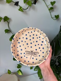 a hand holding up a blue and white plate with a dragonfly design on it