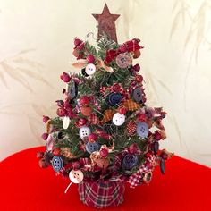 a small christmas tree decorated with buttons and plaid ribbon on a red tablecloth covered surface