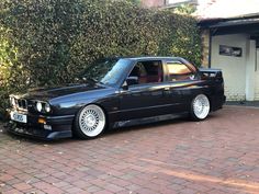 a black bmw is parked in front of a building with bushes on the side of it