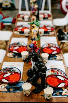 the table is set with red and black plates, silverware, and figurines