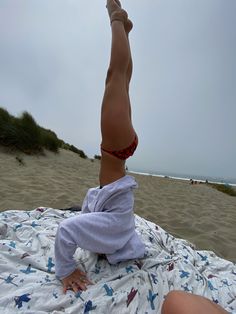 a woman laying on top of a beach next to the ocean with her legs in the air