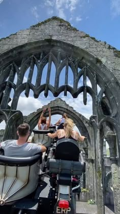 two people riding on a motorcycle in front of an old building with arches and stone walls