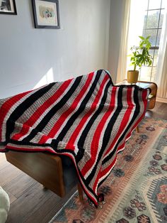 a red, black and white striped blanket sitting on top of a wooden bench next to a potted plant