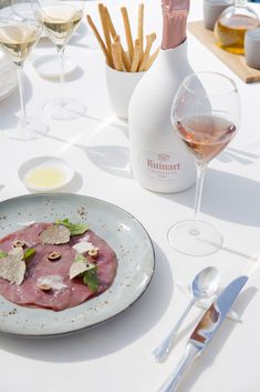 a white table topped with glasses of wine and plates filled with food next to utensils