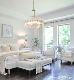 a bedroom with white furniture and chandelier hanging from the ceiling in front of two windows