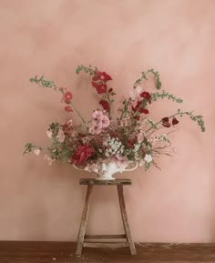 a vase filled with lots of flowers sitting on top of a wooden table next to a pink wall