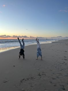 two people doing handstands on the beach at sunset