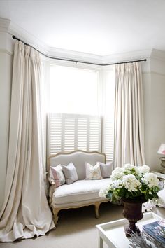 a living room filled with furniture and white flowers on top of a window sill