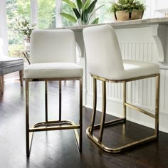 two white chairs sitting next to each other on top of a hard wood floor in front of a window