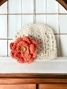 a crocheted hat with a red flower on the front sits on a shelf