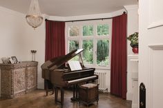 a grand piano sitting in the corner of a room with red curtains and a chandelier