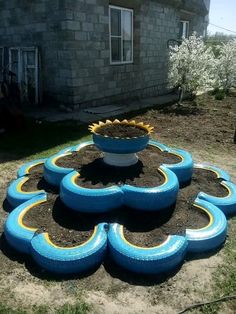 there is a large flower pot in the middle of some dirt and grass with blue tires around it