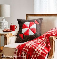 a red and white throw pillow sitting on top of a chair next to a lamp