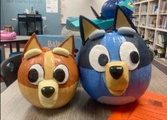 two pumpkins decorated to look like cartoon characters are sitting on a table in front of bookshelves