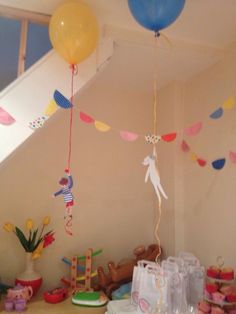 balloons and streamers are hanging from the ceiling above a table filled with toys, cake and other items