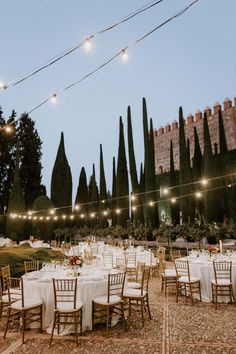 an outdoor dining area with tables and chairs, lights strung from the ceiling and trees in the background