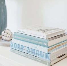 a stack of books sitting on top of a white shelf next to a sea shell