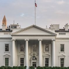 the white house is surrounded by hedges and bushes with an american flag on top of it