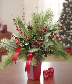 a red vase filled with greenery and pine cones on top of a wooden table