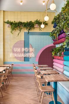 a colorful restaurant with lots of plants hanging from the wall and wooden tables in front of them