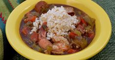 a yellow bowl filled with stew and rice on top of a green table cloth next to a fork